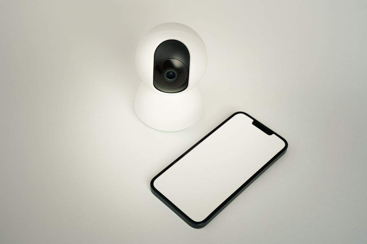 About A smart home security camera paired with a blank smartphone on a white background.